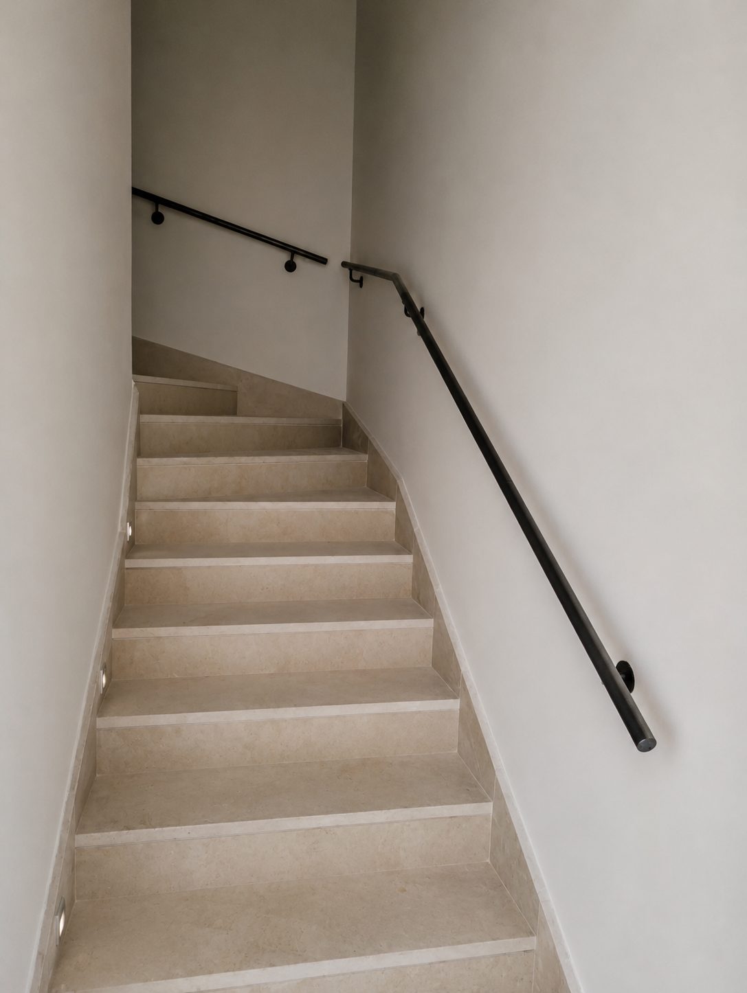 Minimal black steel wall-mounted handrail on stone stairs